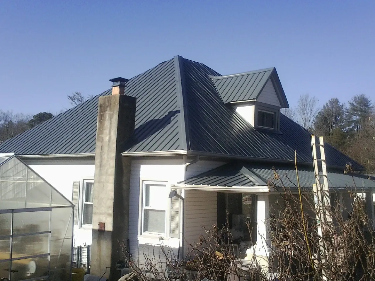 Dark blue standing seam metal roof on a white farmhouse with dormer — Slate & Tile Roof Repair by Roofing Brothers in Kendrick