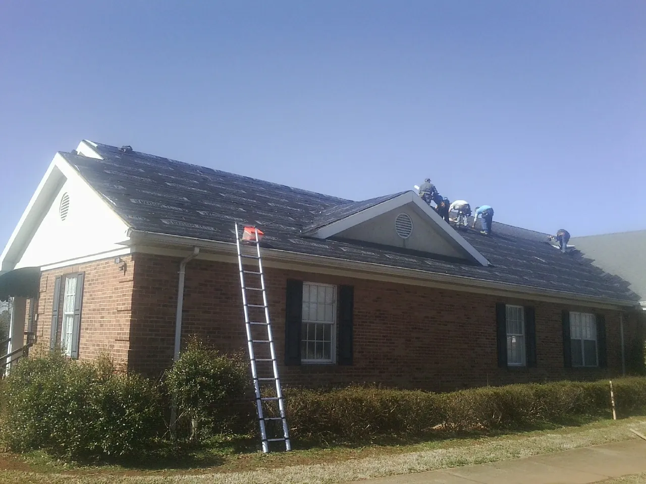 Crew tearing shingles off a brick ranch roof with a ladder set — Metal Roof Repair work by our crew in Kendrick
