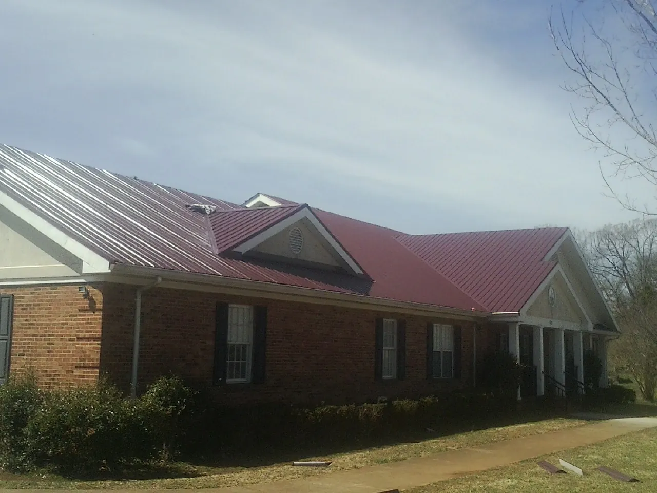 Red metal roof with gabled entries on a long brick building, from a Hail Damage Roof Repair job in Kendrick