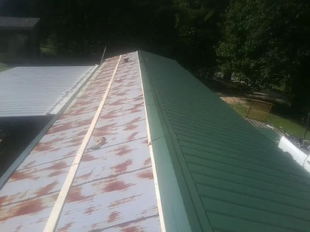 Old rusted panels beside newly installed green metal roofing — Wind Damage Roof Repair by Roofing Brothers in Kendrick