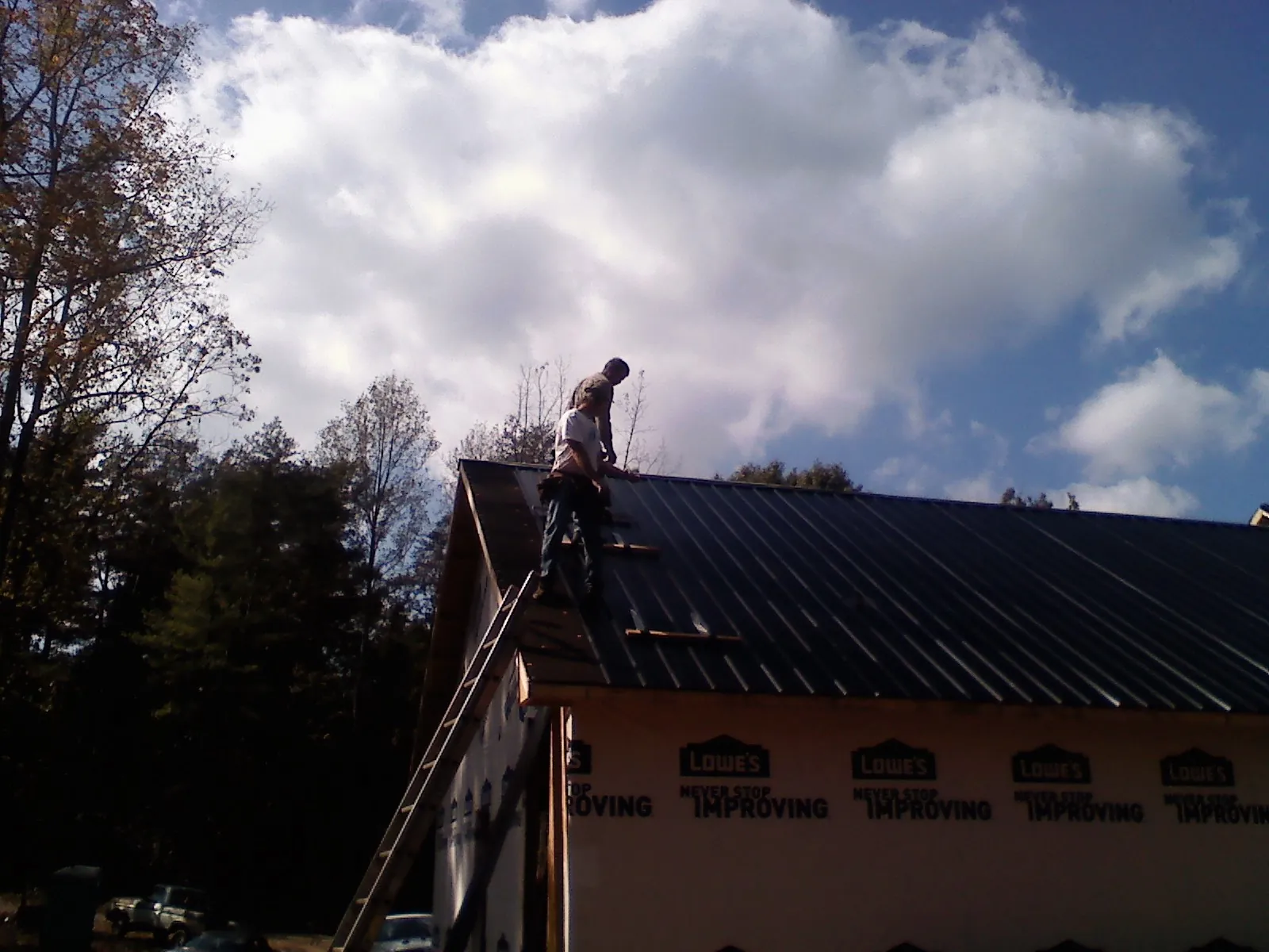 Roofer fastening dark metal panels high against a cloudy sky, from a Roof Inspection job in Kendrick